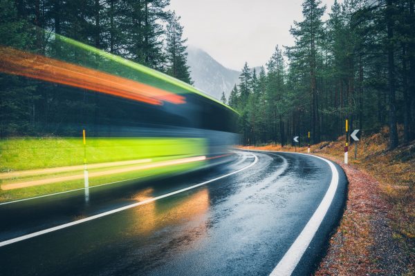 Blurred green bus on the road in autumn forest in rain